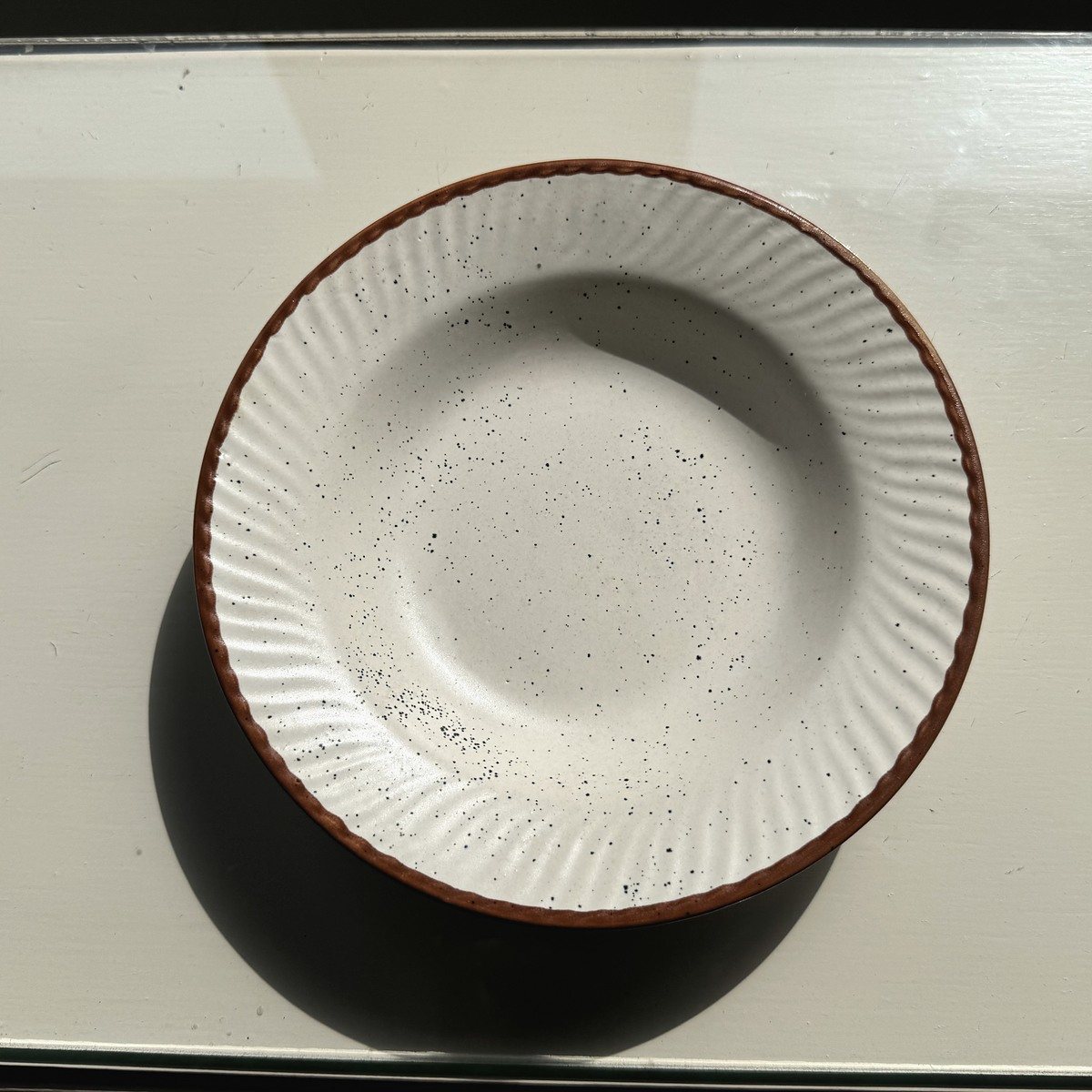 Cream ceramic plate with subtle ridges and a warm rust rim