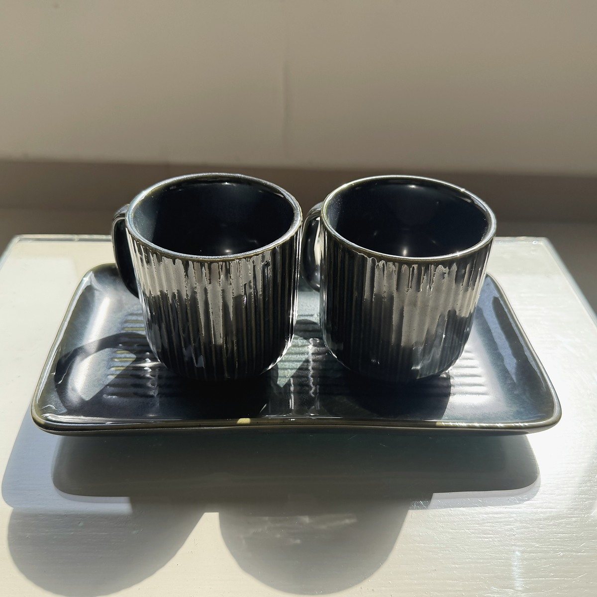 Two ribbed charcoal ceramic mugs arranged on a matching tray